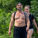 Фотография мужчины с большой татуировкой на груди и плече, идущего по улице. Татуировка выполнена в черно-белых тонах и имеет сложный, детализированный рисунок.