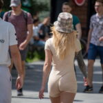 Фотография девушки в бежевом комбинезоне и шляпе с татуировкой на руке, идущей по улице. Современный стиль и красивый рисунок татуировки.