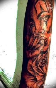 Фото татуировки с изображением портрета женщины и розы на руке. Рисунок выполнен в реалистичном стиле с использованием черных и серых оттенков.