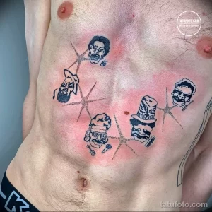 Фото тату на груди и животе с изображением нескольких мистических масок и звезд. Рисунок выполнен в черном цвете.