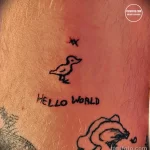 Фото тату с изображением маленькой птички и надписи "Hello World", выполненной в минималистичном стиле на коже. Простой рисунок татуировки.
