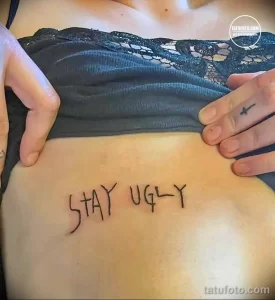 Черно-белое тату на животе с надписью 'Stay Ugly' выполненной от руки. Подчеркнутая небрежность, дерзкий посыл, минималистичный дизайн.