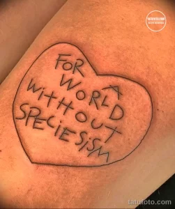 Фото тату на руке с изображением сердца, внутри которого написана фраза "FOR A WORLD WITHOUT SPECIESISM". Черно-белый рисунок татуировки.