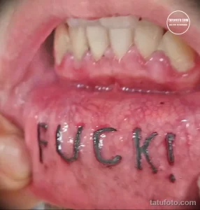 Фото тату надписи 'FUCK!' на внутренней стороне губы. Экстремальный рисунок татуировки, выполненный черными чернилами.