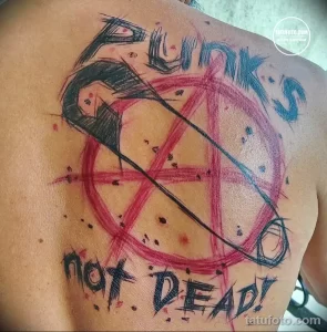 Фото тату на спине: пентаграмма с черепом и надписью 'Not Dead!'. Яркий рисунок татуировки в стиле гранж с использованием красного и черного цветов.