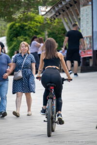 Фото тату на спине девушки, едущей на велосипеде по городской улице. Видна небольшая татуировка в области поясницы.