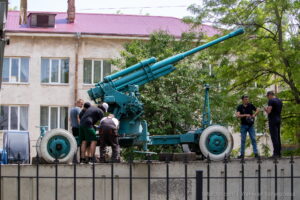 Фото старинной пушки на постаменте. Зеленая окраска, массивные колеса, детализированная конструкция. Исторический памятник на открытом воздухе.