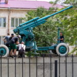 Фото старинной пушки на постаменте. Зеленая окраска, массивные колеса, детализированная конструкция. Исторический памятник на открытом воздухе.