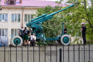 Фото старинной пушки на постаменте. Зеленая окраска, массивные колеса, детализированная конструкция. Исторический памятник на открытом воздухе.
