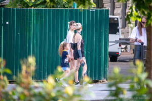 Фотография уличной татуировки на ноге женщины, идущей с ребенком. Видны красочные рисунки, включая цветы и абстрактные узоры. Яркий пример современной татуировки.