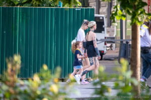 Фотография татуировки на ноге с изображением черепа и цветов, выполненной в реалистичном стиле. Женщина идет по улице на фоне зеленой стены.