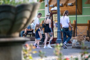 Фотография татуировки на ноге с изображением черепа и цветов, выполненной в реалистичном стиле. Женщина идет по улице.