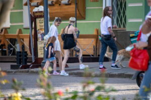 Фотография татуировки на ноге с изображением черепа и цветов, выполненной в реалистичном стиле. Женщина идет по улице.