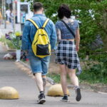 Фото уличной татуировки на девушке. Виден геометрический узор на спине и татуировка на икре ноги. Девушка в джинсовых шортах и клетчатой юбке.