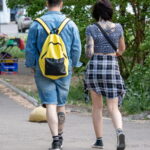 Фотография пары, идущей по улице. У мужчины и женщины видны татуировки на руках и ногах. На ноге мужчины изображен череп.