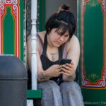 Фотография девушки с татуировками на руках и груди, сидящей на скамейке и смотрящей в телефон. Видны татуировки с надписью и абстрактными узорами.
