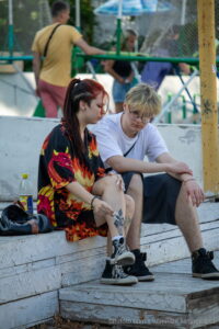 Фото двух людей с татуировками на бедрах, сидящих на ступеньках, погруженных в свои мысли, на фоне городской улицы.