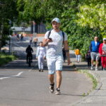 Фотография мужчины, идущего по улице с татуировкой на руке. Солнечный день и городская среда.