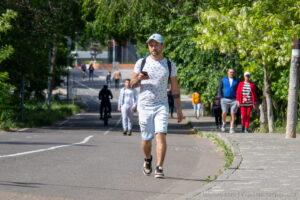Фотография мужчины, идущего по улице с татуировкой на руке. Солнечный день и городская среда.