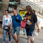 Фотография мужчины с татуировкой на руке, идущего по улице в окружении людей и городской инфраструктуры.