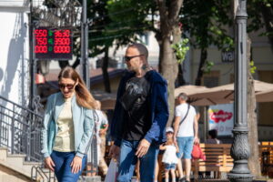 Фото мужчины с татуировкой на шее, одетого в куртку и очки, на фоне городской улицы.