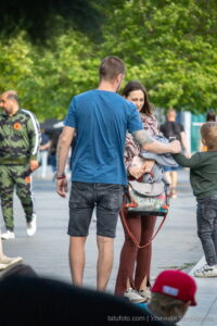 Фото мужчины с татуировкой на руке, держащего за руку ребенка. Татуировка выполнена в темных тонах и состоит из геометрических узоров и надписей.