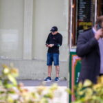 Фото тату на руке мужчины, смотрящего в телефон на улице. Видна небольшая татуировка, детализированная и выполненная в темных тонах.