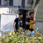 Фотография мужчины с татуировкой на руке, идущего по улице. Татуировка выполнена в черно-серых тонах и изображает сложный рисунок.