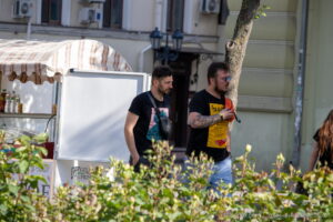 Фотография мужчины с татуировкой на руке, идущего по улице. Татуировка выполнена в черно-серых тонах и изображает сложный рисунок.