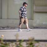 Фотография мужчины с татуировками на руках и плечах, одетого в рубашку с принтом черепов. Современный городской стиль.