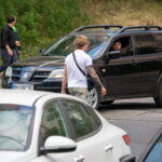 Фотография мужчины с татуировкой на руке, стоящего рядом с черным автомобилем. Видна часть лица мужчины и интерьер автомобиля.
