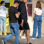 Фото тату на руке мужчины: темный рисунок, возможно, в виде узора или символа. Видна татуировка на руке, когда мужчина разговаривает с другим человеком.