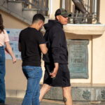 Фото тату на икре мужчины: темный рисунок, возможно, в виде узора или символа. Видна татуировка на икре, когда мужчина стоит возле памятника.