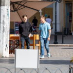 Фотография мужчины с татуировкой на предплечье, идущего по улице. Татуировка выполнена в темных тонах и имеет сложный узор. Уличная татуировка, современный стиль.