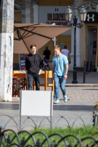 Фотография мужчины с татуировкой на предплечье, идущего по улице. Татуировка выполнена в темных тонах и имеет сложный узор. Уличная татуировка, современный стиль.