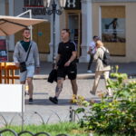 Фото мужчины с татуировками на предплечье и плече. Рисунок татуировки выполнен в темных тонах. Мужчина одет в черную футболку и шорты.