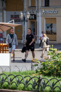Фото мужчины с татуировками на предплечье и плече. Рисунок татуировки выполнен в темных тонах. Мужчина одет в черную футболку и шорты.