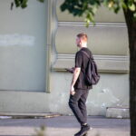 Фотография мужчины, идущего по улице с рюкзаком, на руке которого видна татуировка. Тату выполнено в темных тонах.