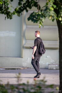Фотография мужчины, идущего по улице с рюкзаком, на руке которого видна татуировка. Тату выполнено в темных тонах.