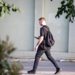 Фотография мужчины, идущего по улице с рюкзаком, на руке которого видна татуировка. Тату выполнено в темных тонах.