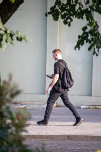 Фотография мужчины, идущего по улице с рюкзаком, на руке которого видна татуировка. Тату выполнено в темных тонах.