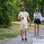 Фотография мужчины в белой футболке и шортах с татуировкой на руке, идущего по улице с женщиной. Видна часть татуировки на предплечье.