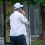 Фотография мужчины в белой рубашке и кепке с татуировкой на руке, разговаривающего по телефону. Мужественный образ и интересный рисунок татуировки.