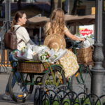 Фотография двух девушек на велосипеде, везущих корзины с цветами. Идеальное фото для создания романтического настроения и поиска идей для татуировок с изображением цветов и велосипедов.