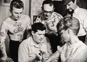 Фотография тату-салона 1950-х годов, где тату-мастер делает татуировку клиенту в окружении других посетителей.