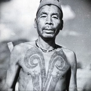 Фотография пожилого мужчины с традиционными татуировками на груди и лице, выполненными в племенном стиле.