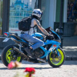 Фотография мотоциклиста на синем спортивном мотоцикле Suzuki, с видимой татуировкой на руке. Динамичная сцена на городской улице.