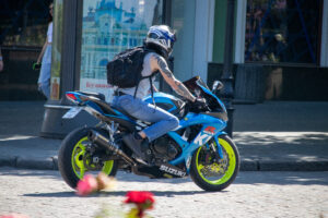 Фотография мотоциклиста на синем спортивном мотоцикле Suzuki, с видимой татуировкой на руке. Динамичная сцена на городской улице.