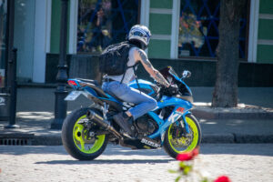 Фотография мотоциклиста на синем спортивном мотоцикле Suzuki, с видимой татуировкой на руке. Динамичная сцена на городской улице.