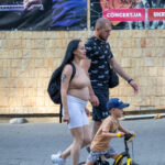 Фотография девушки с татуировкой змеи на плече, идущей по улице с ребенком и велосипедом. Детализированный рисунок татуировки, выполненный в черных тонах, привлекает внимание.